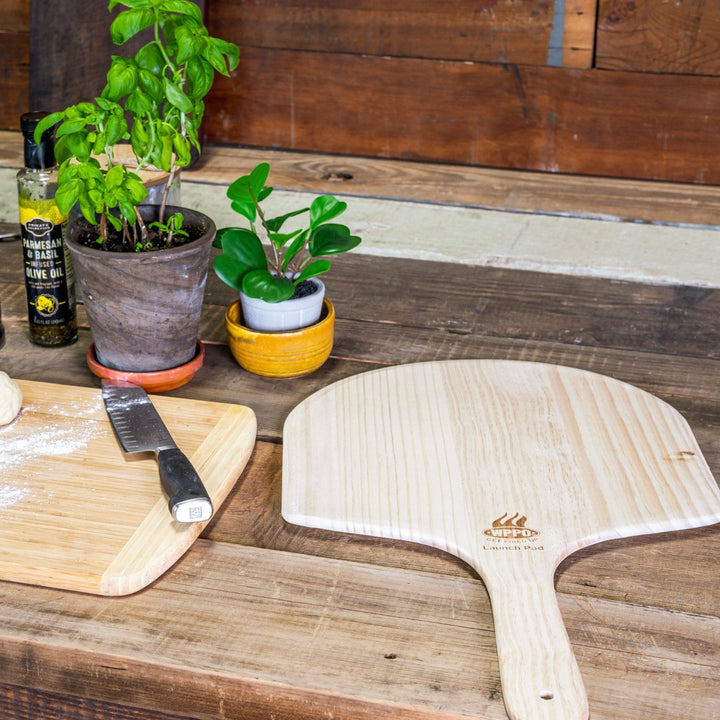 Two light wood pizza peels with rounded paddle and short handles on a tabletop.