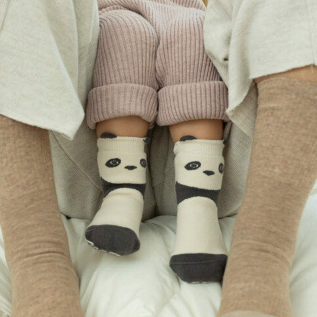 Cream panda-face non-slip socks with ribbed cuffs, worn under light knit pants