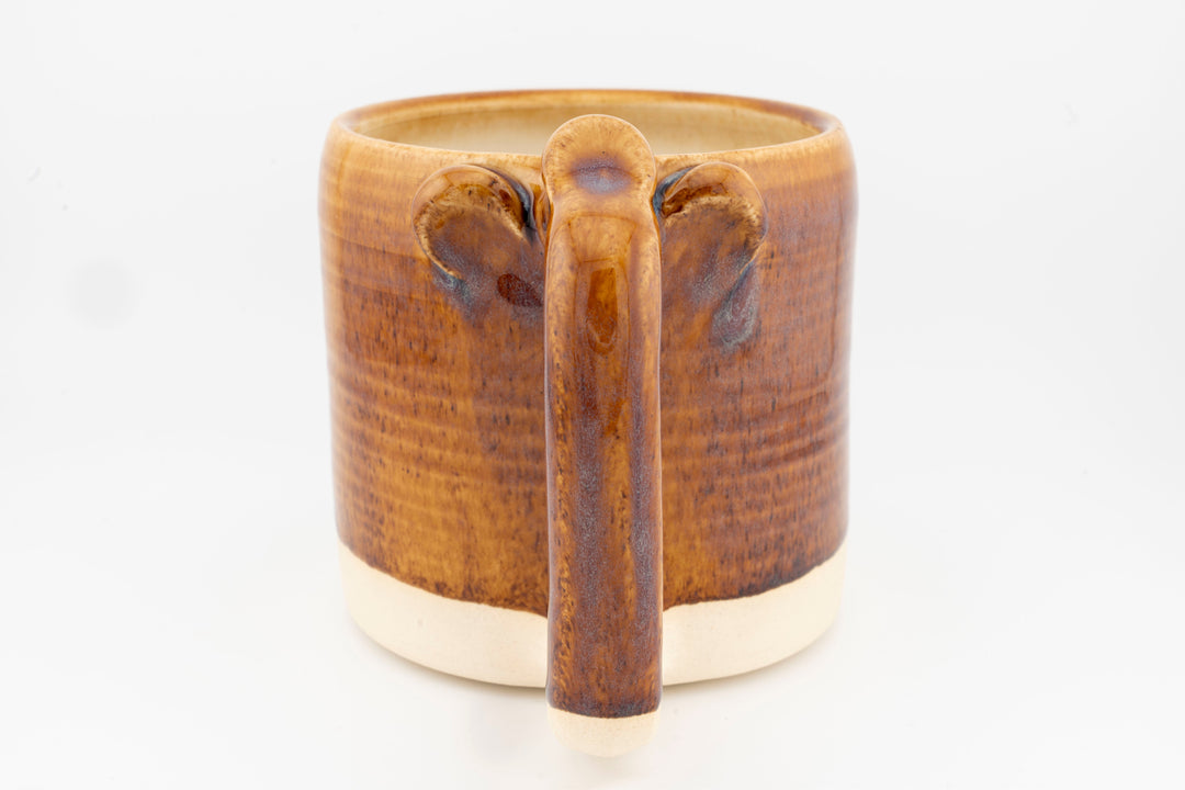 Ceramic mug with brown glaze, front handle detail, and rounded top opening.