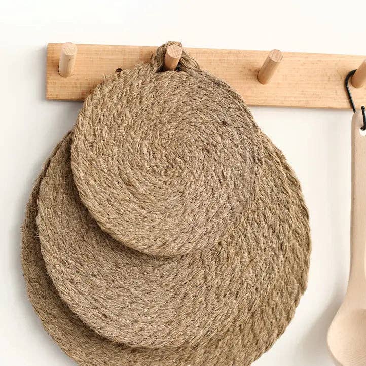 Round woven natural trivet with handle loop, shown hanging on wooden rack