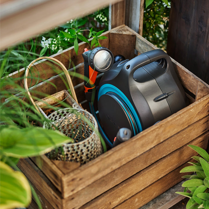 Portable hose reel with black body and blue hose ring, stored in a wooden planter box