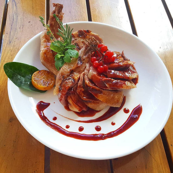White round dinner plate with smooth rim, holds plated meat and sauce.