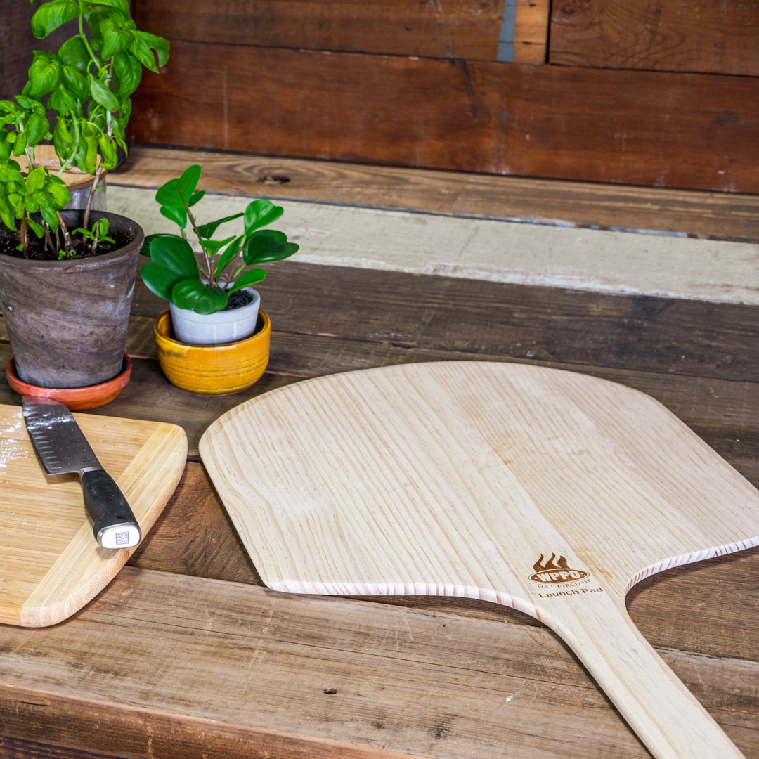 Two light wood long-handled pizza peels with semicircle heads on a table