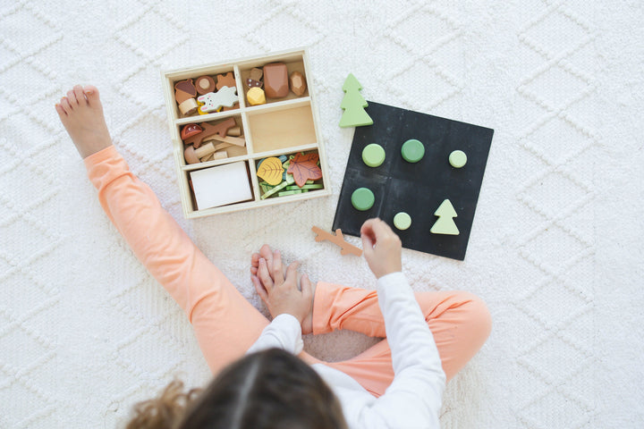 Wooden forest sensory bin with open storage and chalkboard lid, child playing
