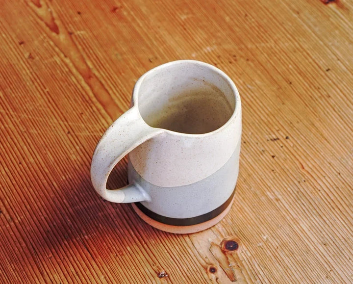 Speckled ceramic mug with handle and dark band around the base