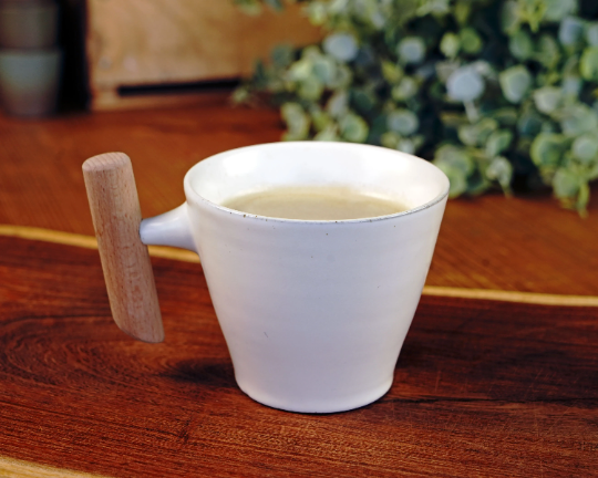 White ceramic mug with wooden handle, filled with a light-colored drink