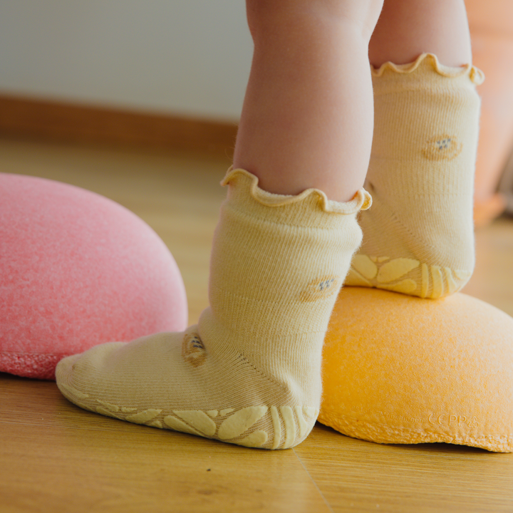 Toddler wearing yellow non-slip socks with ruffled cuffs and patterned grip soles