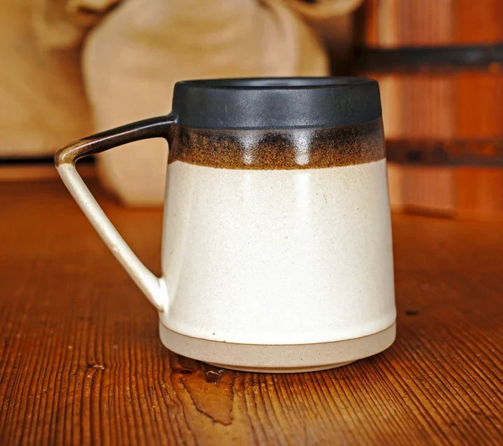 Ceramic mug on wooden table with white body and dark brown band near top