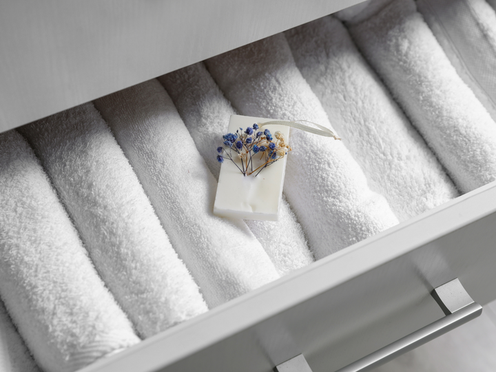 White floral wax sachet with blue dried flowers in a tray lined with towels
