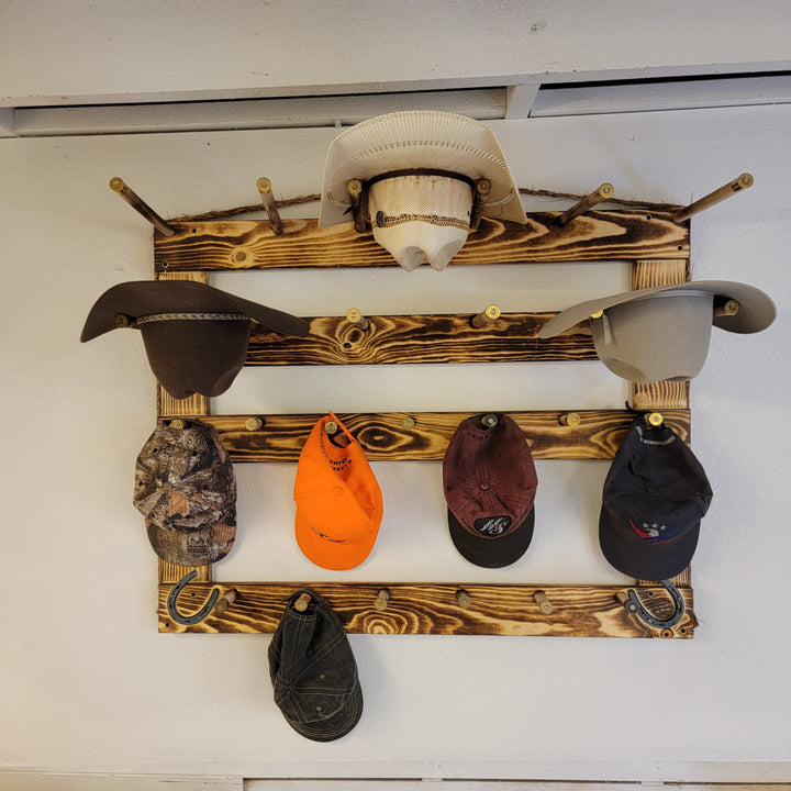 Wall-mounted wood hat rack displaying cowboy hats and several baseball caps on rails