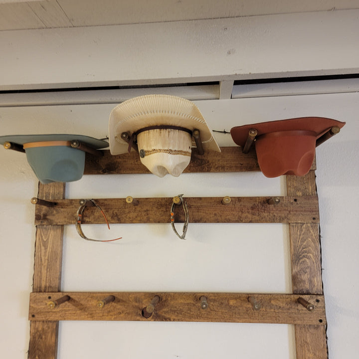 Wooden hat rack display with cream, pale blue, and rust cowboy hats and caps