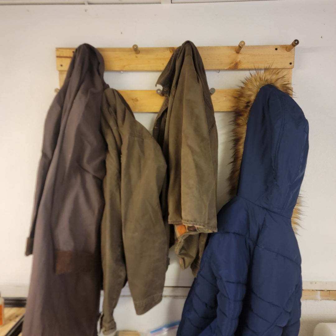 Wall-mounted coat rack with three coats hanging from two rows of hooks