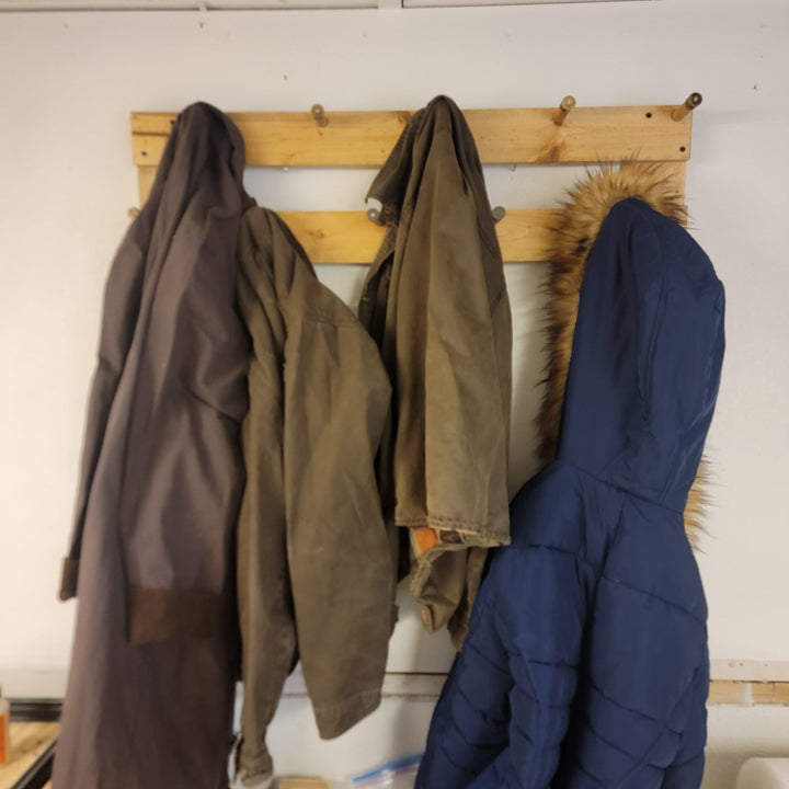 Wall-mounted coat rack with three coats hanging from two rows of hooks