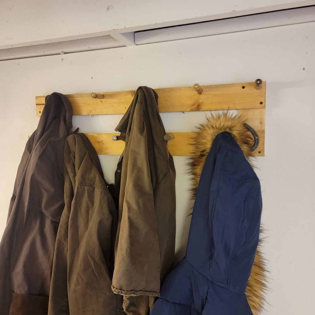 Wall-mounted coat rack with rustic wooden bars and three hanging coats