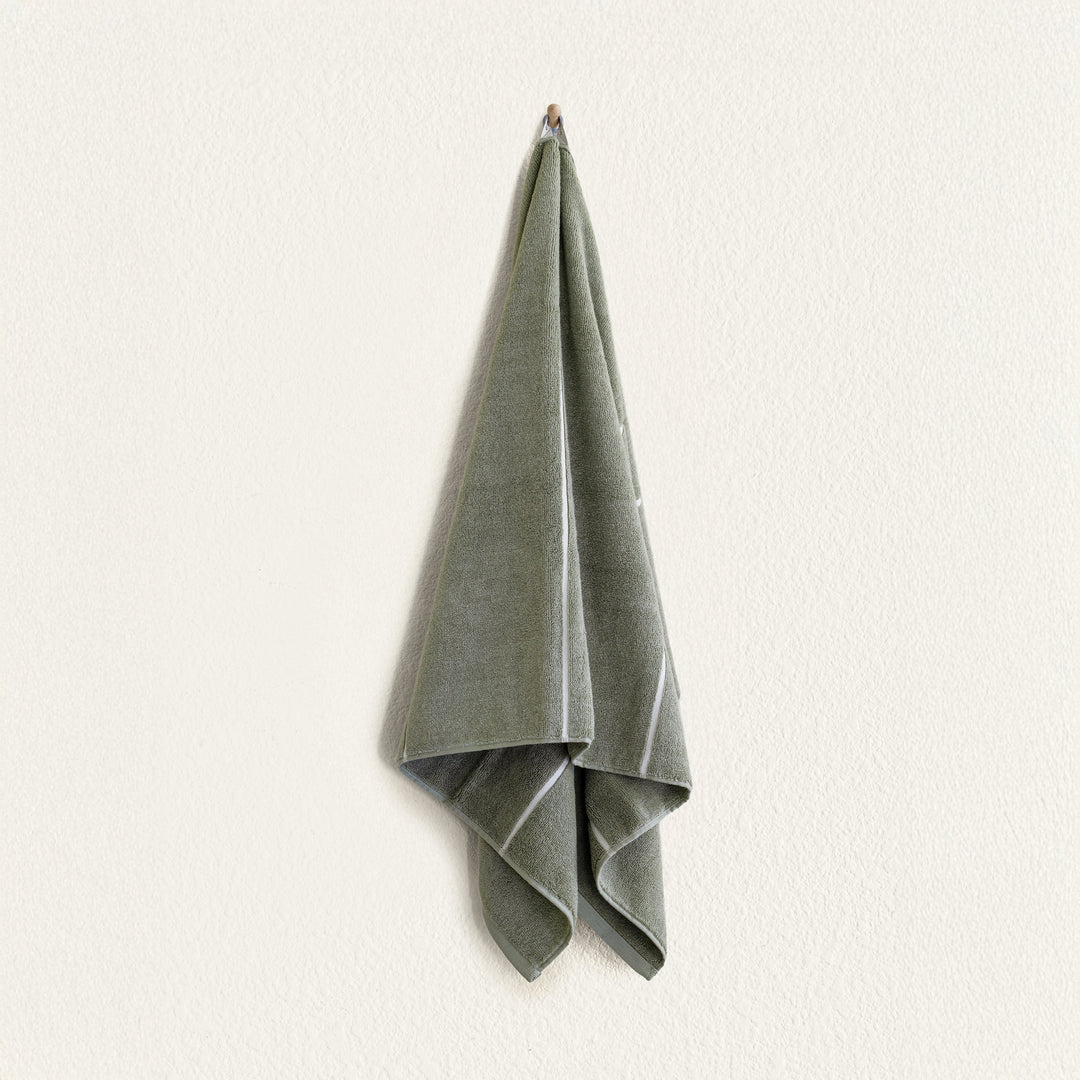 Sage green cotton hand towel with lighter edge stitching, folded and hanging.
