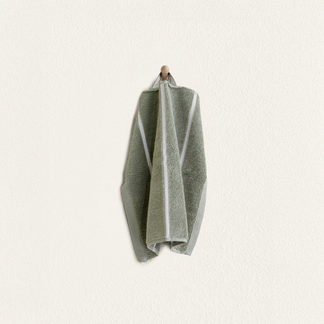 Sage green cotton towel with lighter vertical stripe, folded and tied at the top.