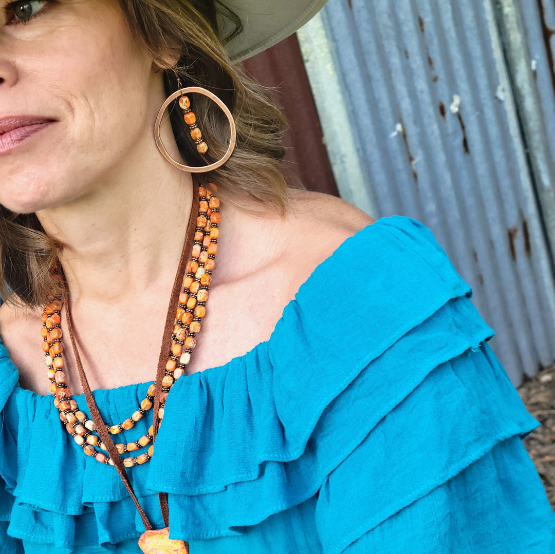 Copper hoop earring with long orange bead dangle and hook back, close-up.