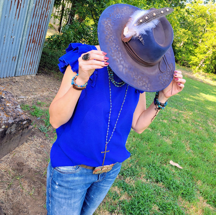Blue leopard-print cowgirl hat with feather and beaded hatband, worn on model