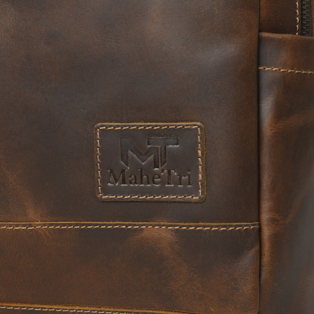 MaheTri logo patch on brown leather backpack with stitched panel and side zipper