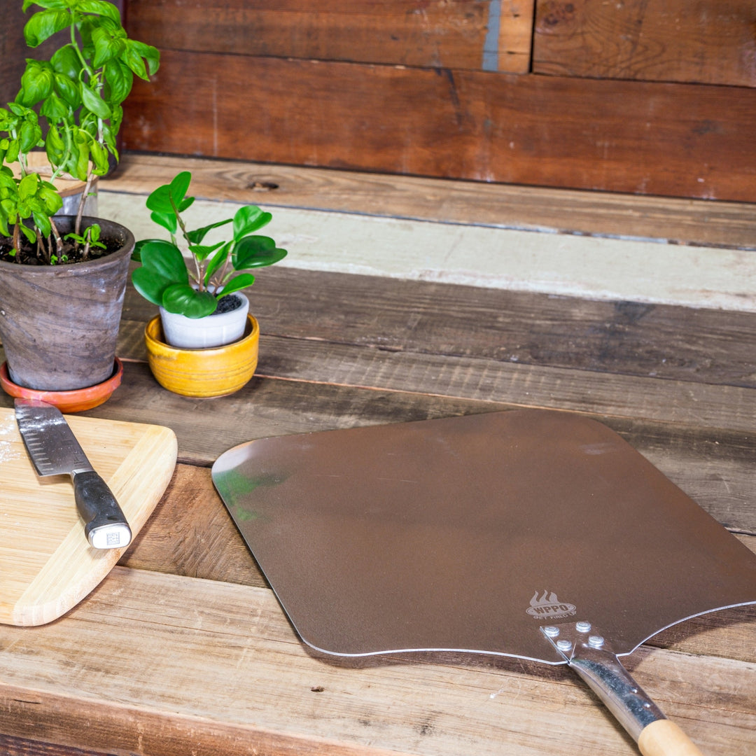 Aluminum pizza peel with wood handle, resting on a wooden surface