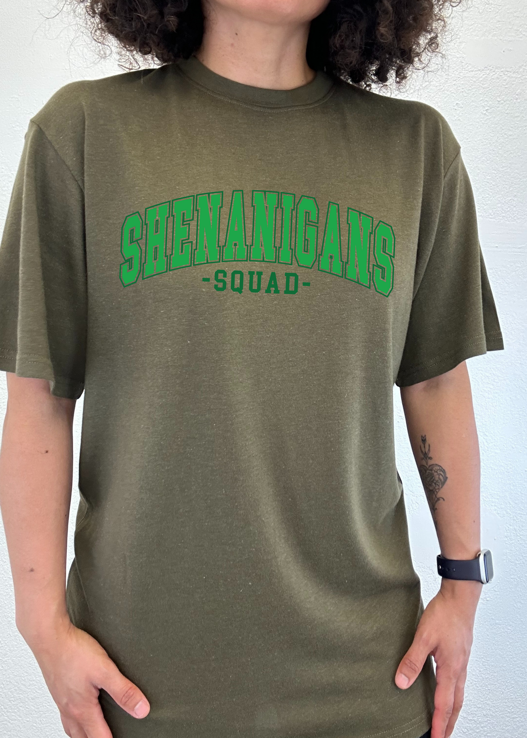 Unisex graphic T-shirt, olive with green “Shenanigans Squad” logo on front.
