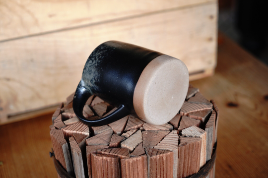 Black stoneware-style mug with tan base, angled view with handle