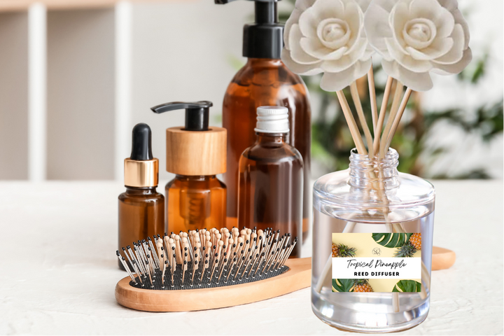 Clear reed diffuser bottle with white rose-tipped reeds next to amber pump bottles