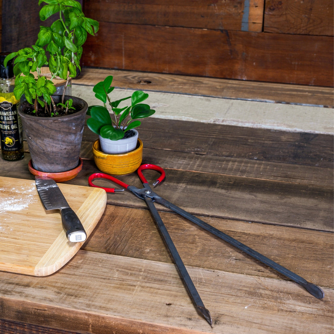 Two forged steel wood pliers on a wooden board with red loop handles