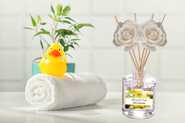 Reed diffuser bottle with wooden reeds next to a rolled towel and rubber duck