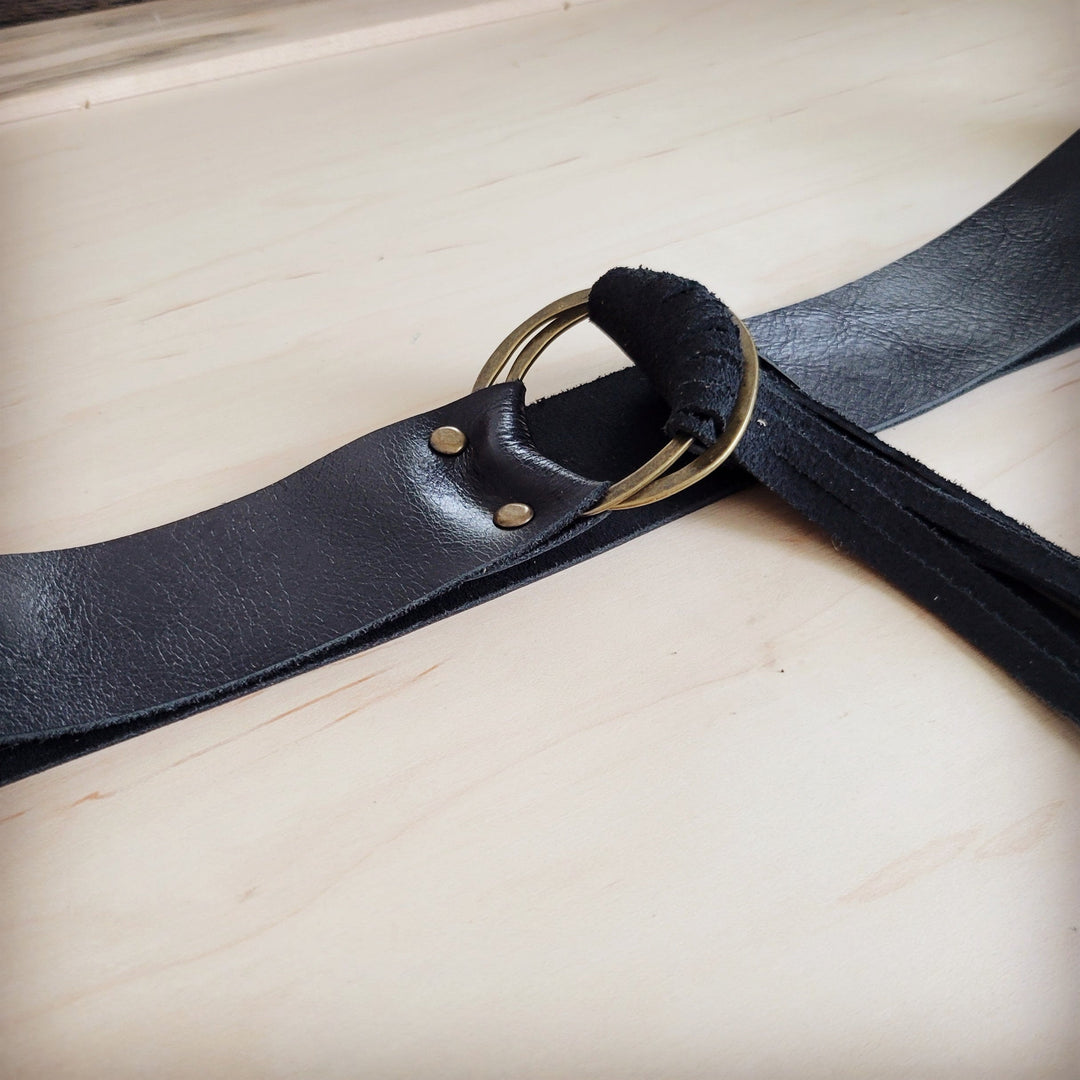 Black leather belt detail with snap studs, round ring buckle, and leather fringe