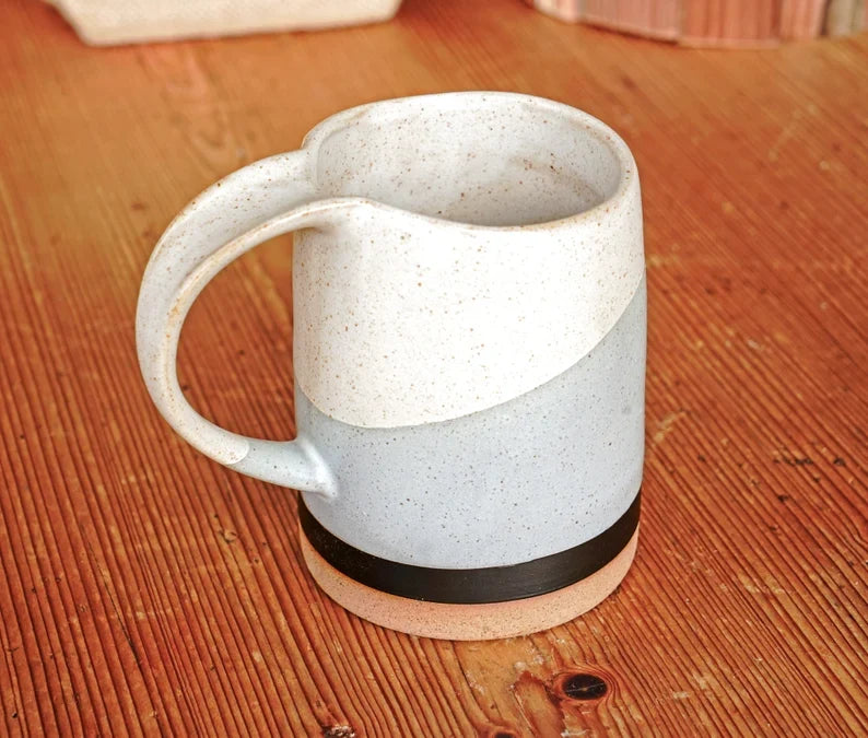 Speckled ceramic mug with side handle and dark band near the bottom