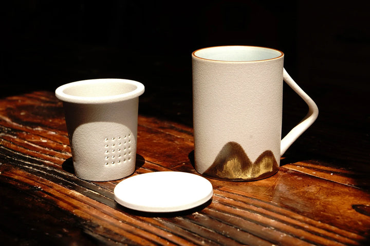 Ceramic tea mug with lid and perforated strainer insert, beige with dark mountain base