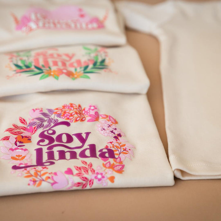 White tee close-up with colorful floral “Soy linda” graphic print