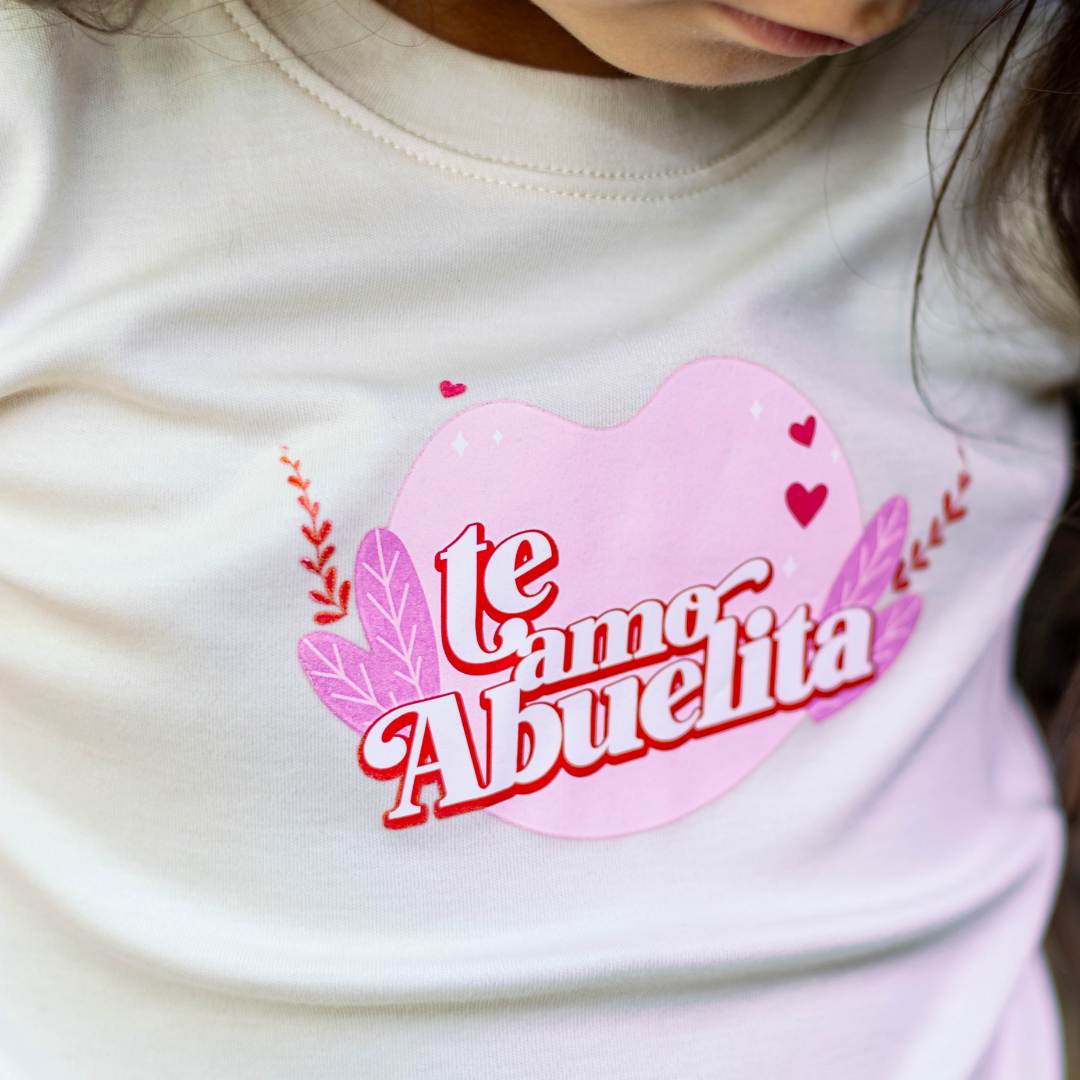 Cream graphic tee with pink heart patch and colorful "Te amo Abuelita" lettering