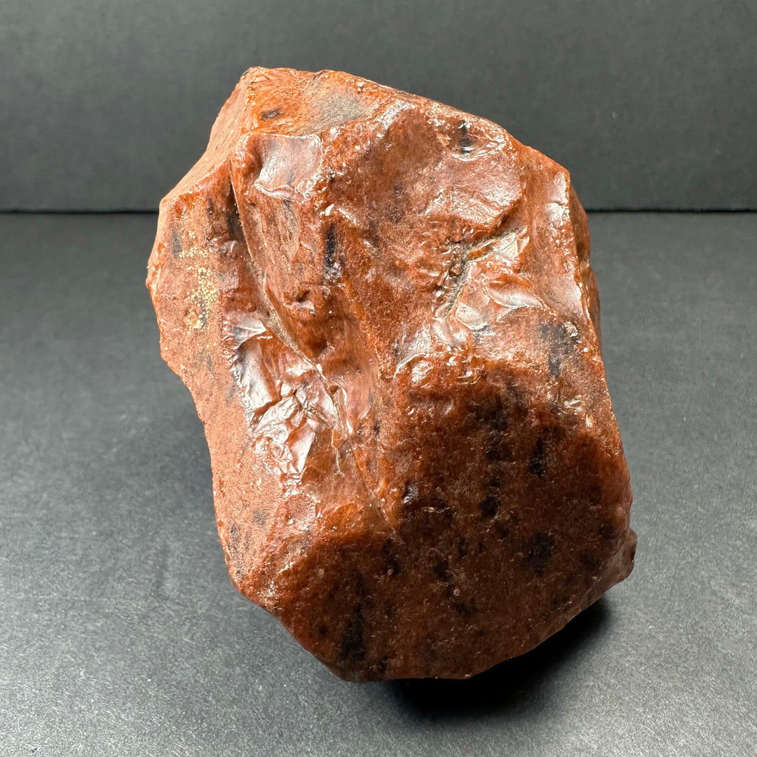 Raw reddish-brown obsidian stone with rough, glassy texture and jagged irregular edges
