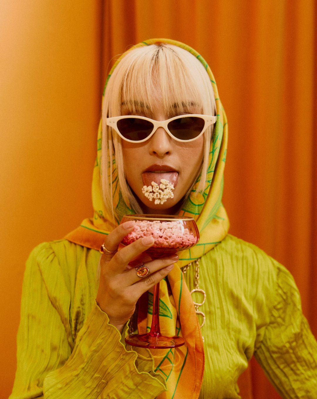 Woman holding a pink popcorn snack pack, wearing sunglasses and a green hoodie
