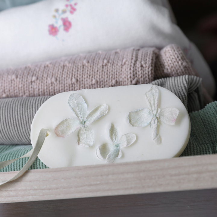 Botanical wax sachet with pale dried flower petals on a white oval, tied with ribbon