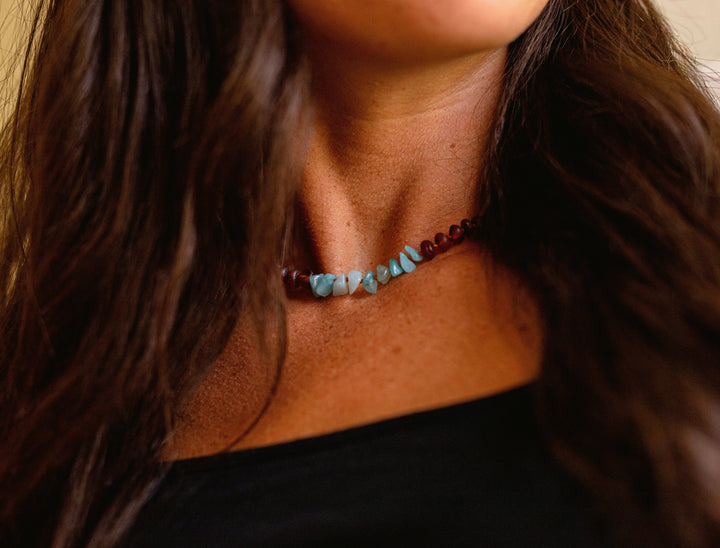 Amber-brown beaded necklace with light blue stone accents worn at the neckline