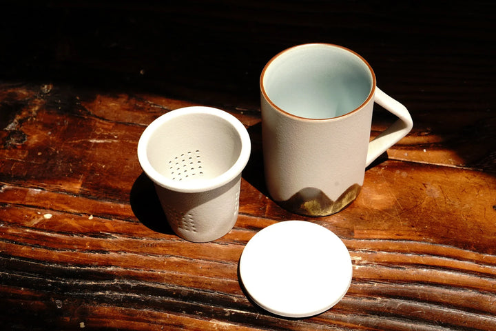 Ceramic tea mug with lid and perforated strainer insert, beige with dark mountain base