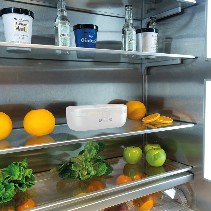 Self-heating lunch box placed on a refrigerator shelf among produce and bottles.