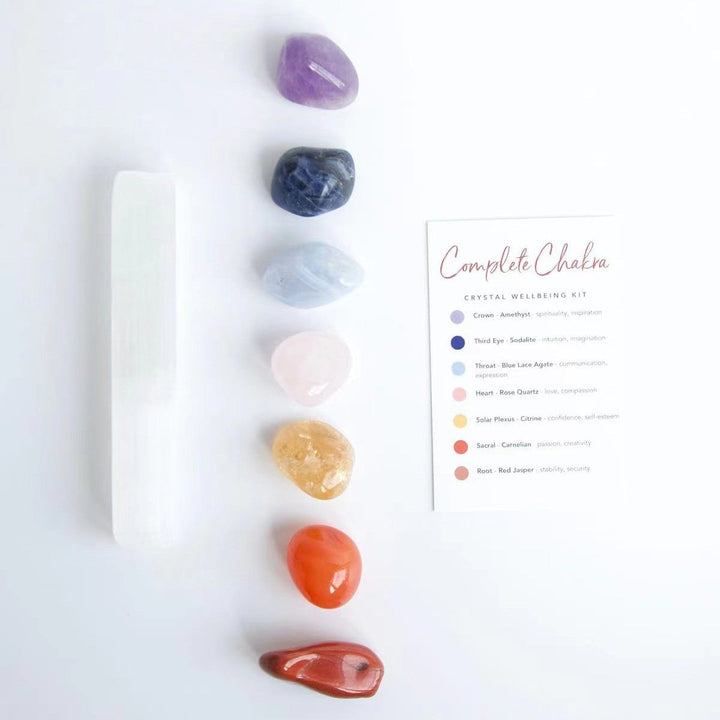 Crystal healing kit with white selenite wand, purple, blue, and orange stones, and card.