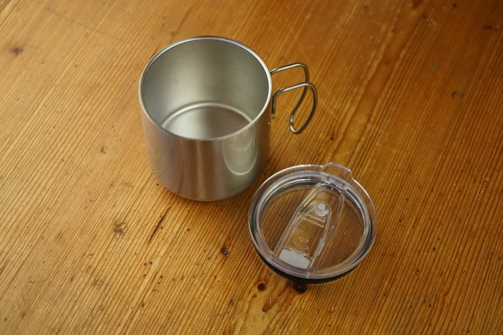 Stainless steel mug with transparent lid, open cup interior, curved side handle.