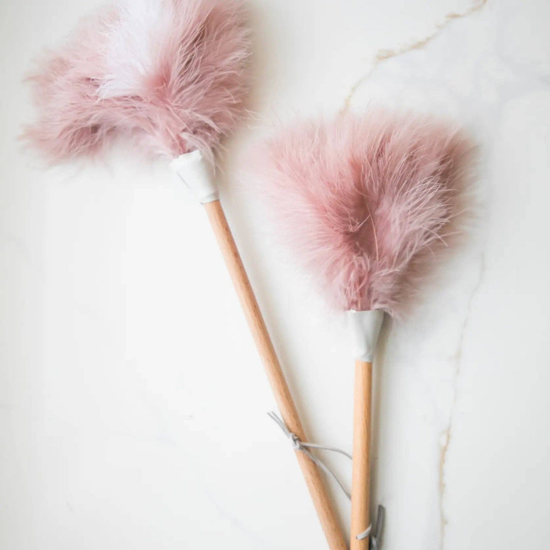 Two pink ostrich feather dusters with soft plume heads and light wooden shafts