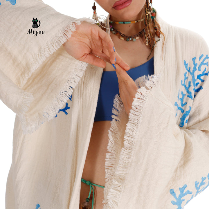 Beige kimono fabric close-up with blue coral embroidery and tassel fringe trim