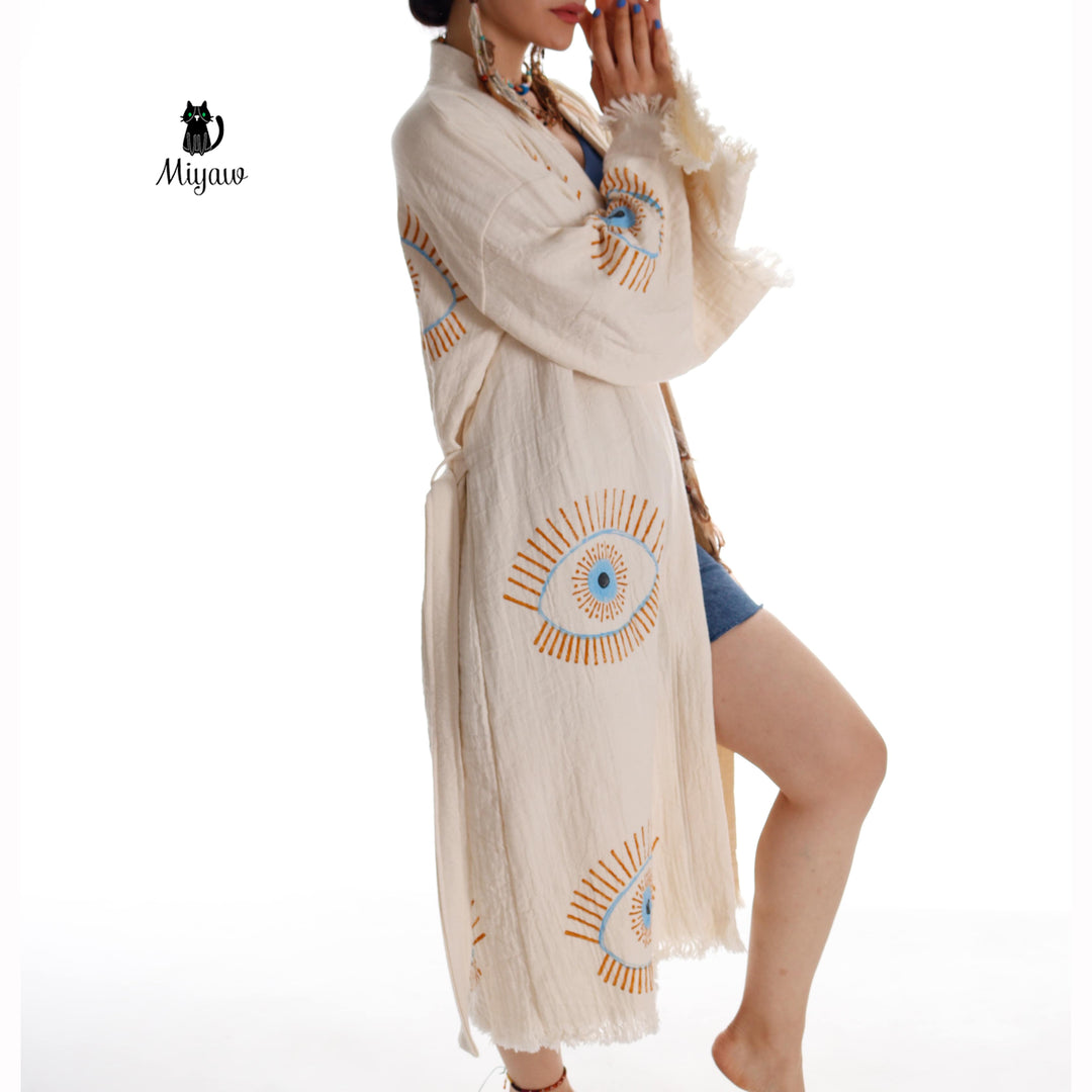 Beige cotton caftan with blue evil-eye motif, belted waist, mid-calf length, fringe hem