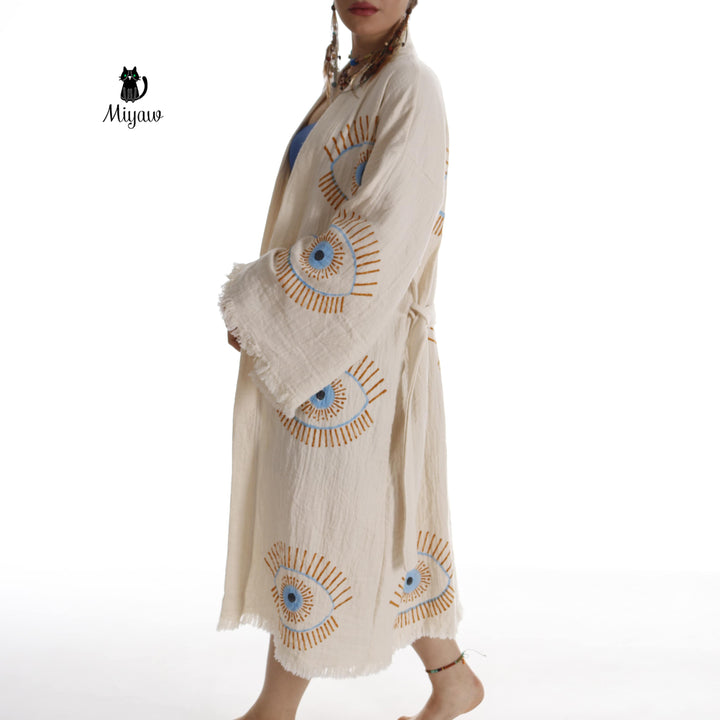 Beige cotton caftan with scattered evil-eye prints, fringe trim, flowing mid-calf hem