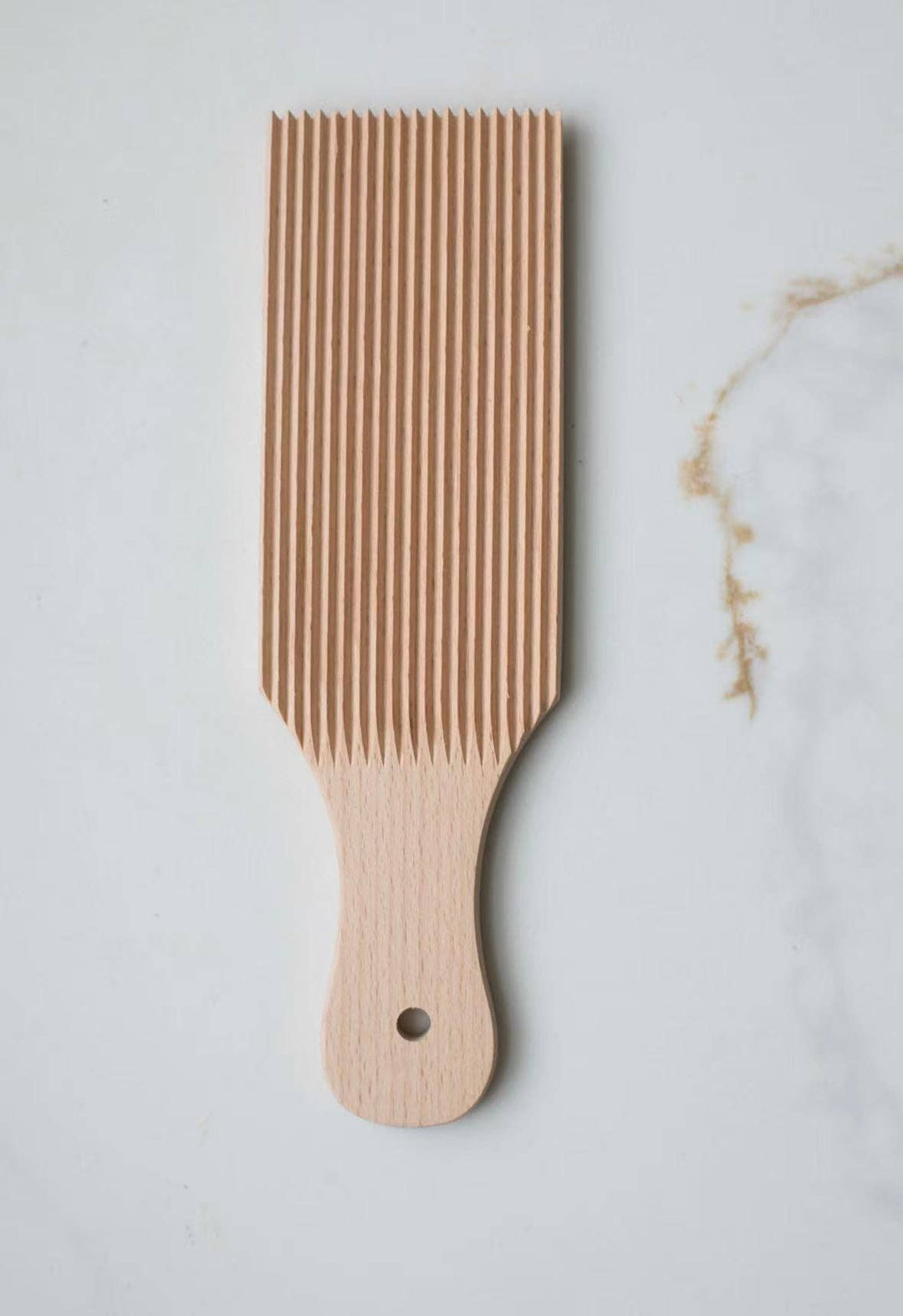 Wooden gnocchi board with evenly spaced vertical ridges and curved handle, black dot