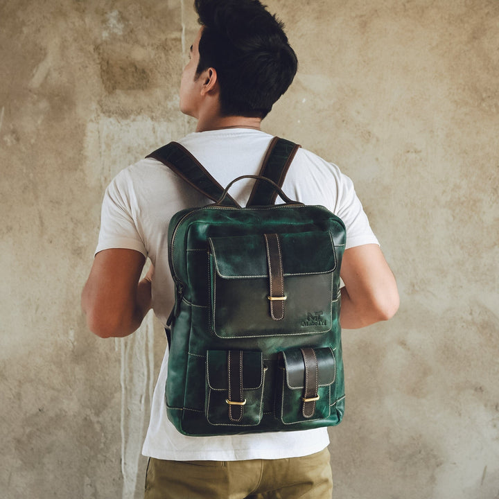 Green leather backpack worn on back with front pockets and adjustable shoulder straps.