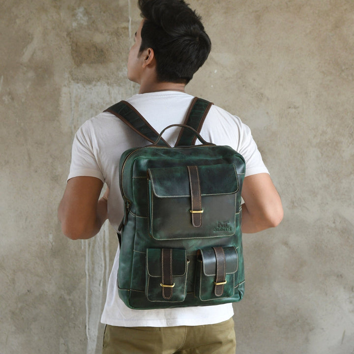 Green leather backpack worn from behind with two front pockets and top handle.