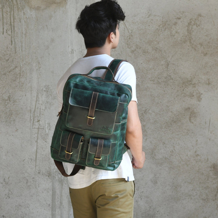 Green leather backpack worn from side, showing flap pocket and brown buckle straps.